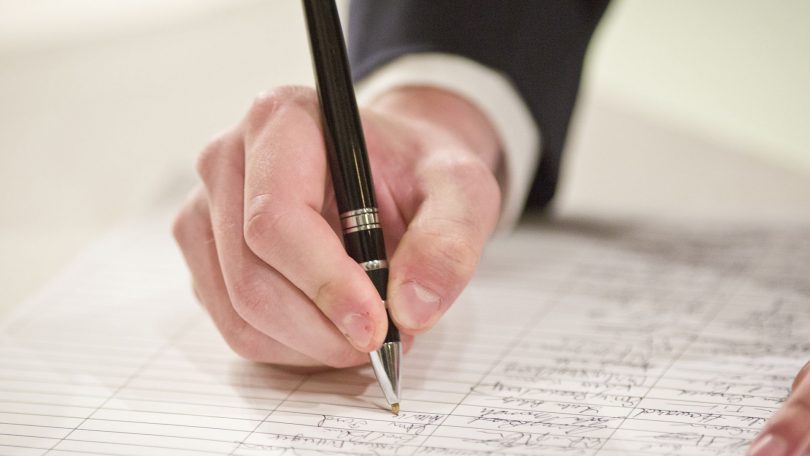 A photograph showing a hand holding a pen and signing a document