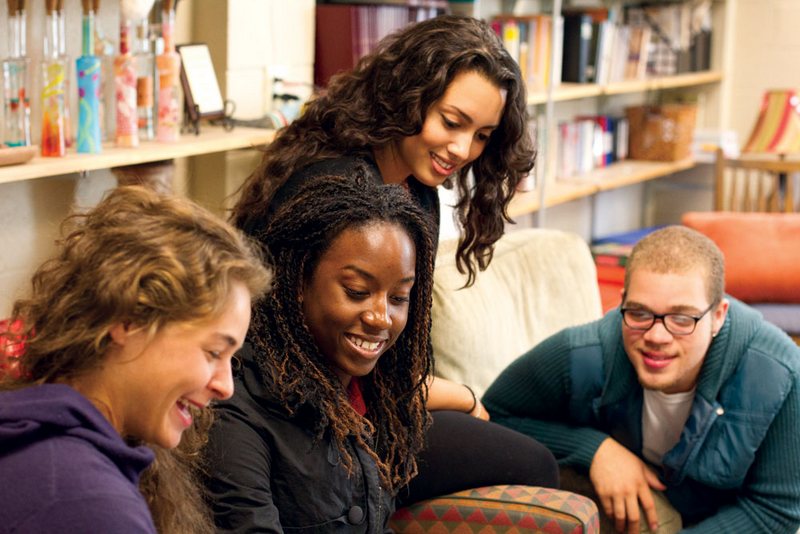 Three students work with a professor in the library