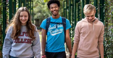 Three Guilford College students walk by the Orangerie at Binford Hall.