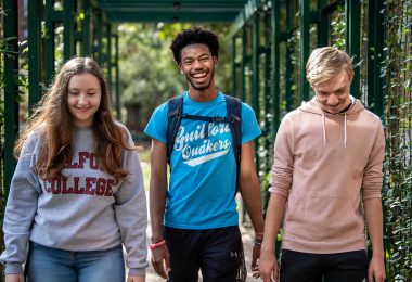 Three Guilford College students walk by the Orangerie at Binford Hall.