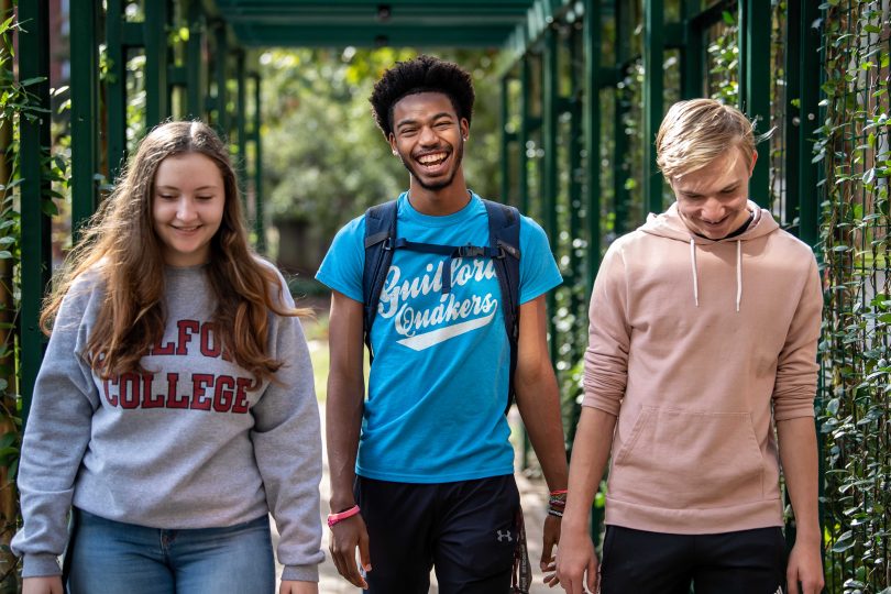 Three Guilford College students walk by the Orangerie at Binford Hall.